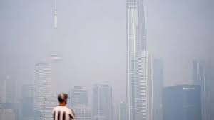 A man in a striped shirt looks at a smoke-filled, hazy skyline in Toronto due to Canadian wildfires.