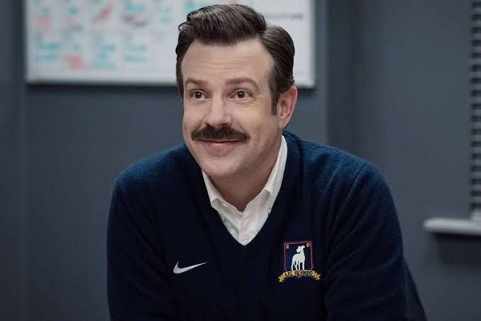 Jason Sudeikis on the set of Ted Lasso as the character Ted holding a soccer ball.