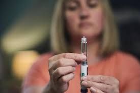 Close up of a person holding an injector pen for weight loss medication with their face blurred in the background.
