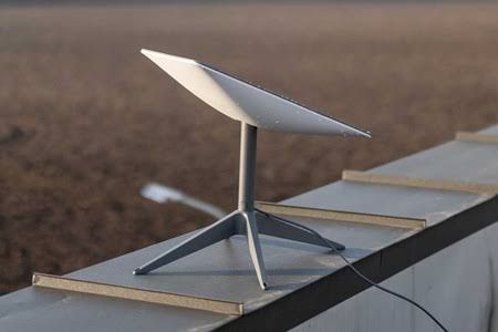 A Starlink satellite dish antenna mounted on a tripod in a field with a blurred rural landscape in the background.