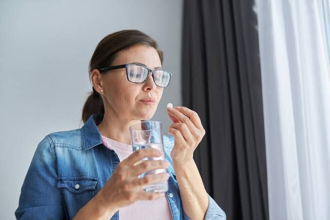 Close up of a woman showing an allergic rash on her neck while holding a prescription medicine bottle.