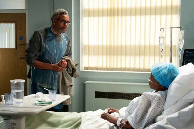 Darnell Larson Jr wearing a blue apron in a hospital ward during a scene from EastEnders.