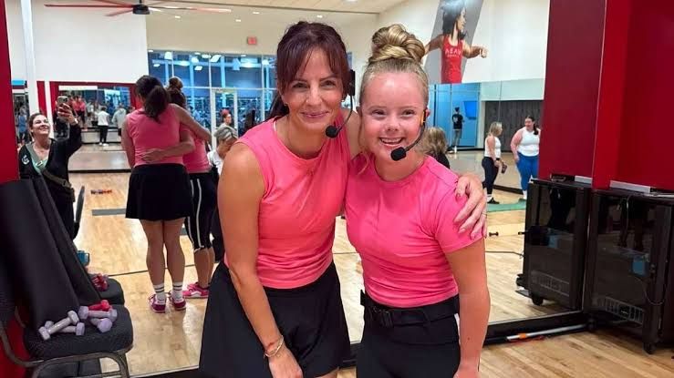 Aubry Alldredge wearing a microphone and teaching an UpBeat Barre fitness class to a group in a studio.