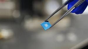 Close-up of a semiconductor chip prototype under a microscope lens in a research laboratory setting.