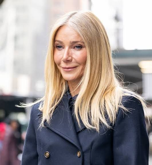 Gwyneth Paltrow standing on a red carpet while smiling during a formal industry event.