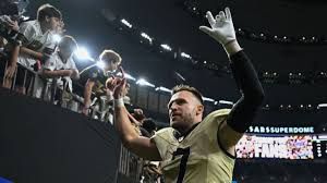 Taysom Hill standing on the sidelines at the Caesars Superdome wearing his New Orleans Saints uniform.