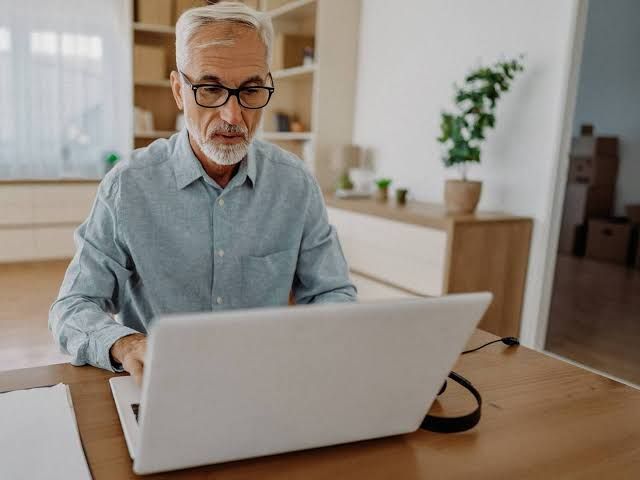 Close up of an elderly person calculating retirement expenses with a calculator and pension documents on a desk.