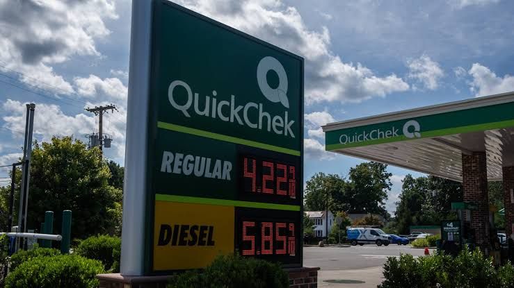 A frustrated driver standing at a New Jersey gas station while monitoring rising fuel prices on the digital display.
