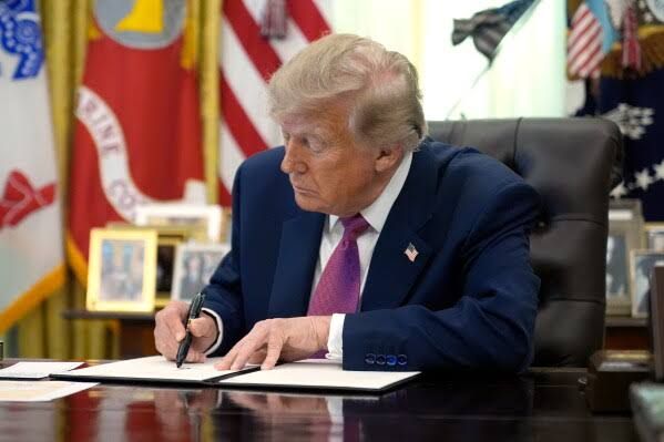 President Donald Trump holding a signed executive order in the Oval Office regarding the renaming of Lake Ontario.