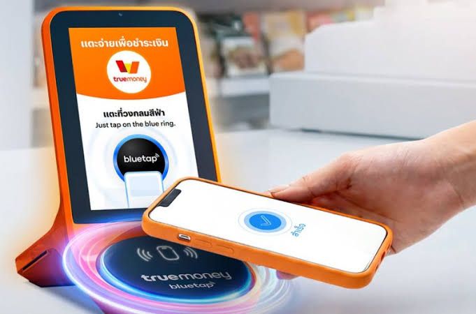 TrueMoney staff member demonstrating mobile tap-to-pay technology at a retail contactless terminal.