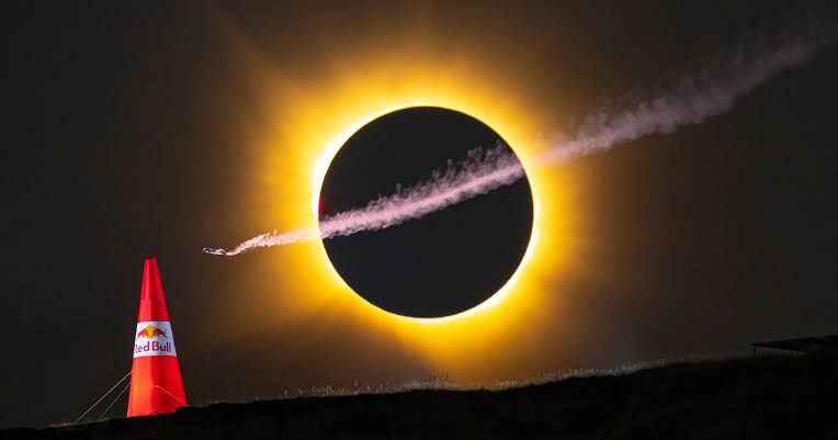 Wingsuit pilot flying in front of a total solar eclipse above a Red Bull pylon during the August 2026 event in Spain.