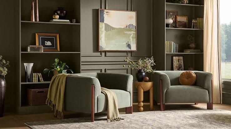 A moody hotel lounge featuring olive green walls, velvet furniture, and natural wood accents.