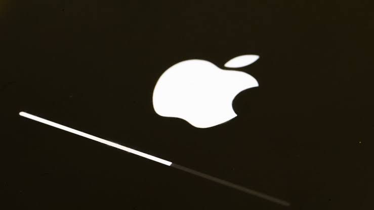Close-up of a person holding an iPhone displaying a software update screen while a blurry Apple logo sits in the background.
