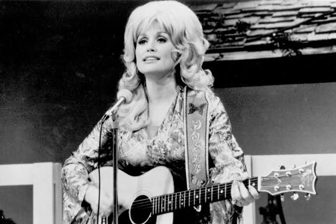 Dolly Parton playing an acoustic guitar during a live country music performance in 1974.