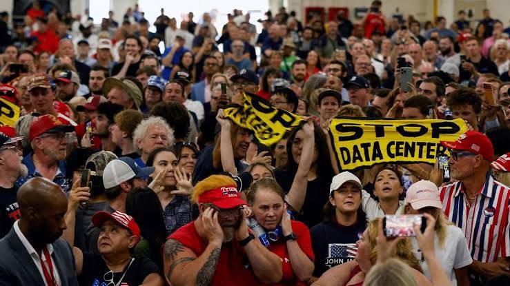 Protesters holding 'Stop data centers' signs during a speech by President Donald Trump.