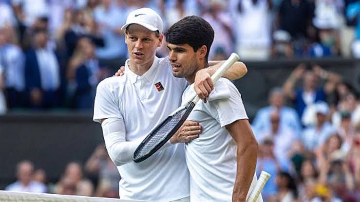 Jannik Sinner and Carlos Alcaraz competing in a professional tennis match on a hard court surface.