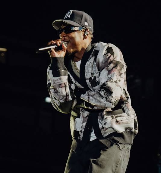 Jay-Z performing on stage in London, holding a microphone and addressing a large crowd.