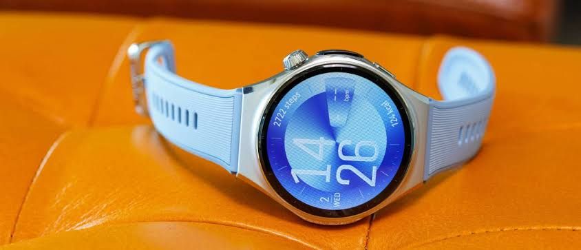 Huawei Watch 6 display showing a clock face on a metallic wrist strap in a studio lighting environment.