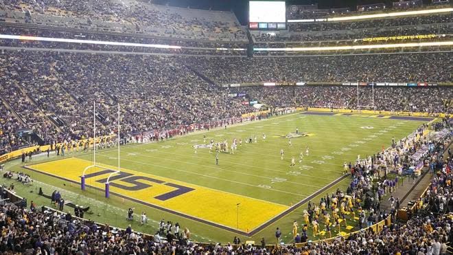 LSU Tiger Stadium viewed from above during a night game with bright field lights and a full crowd in the stands.