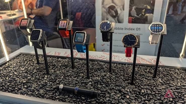 Pebble Time 2 smartwatch displayed on a table next to other wearable devices.