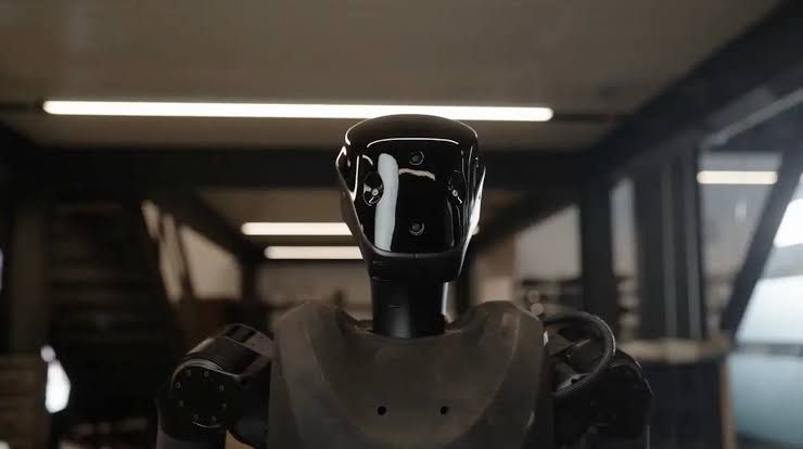 A sleek humanoid robot produced by Foundation standing in a test facility while loading a piece of military ordnance.