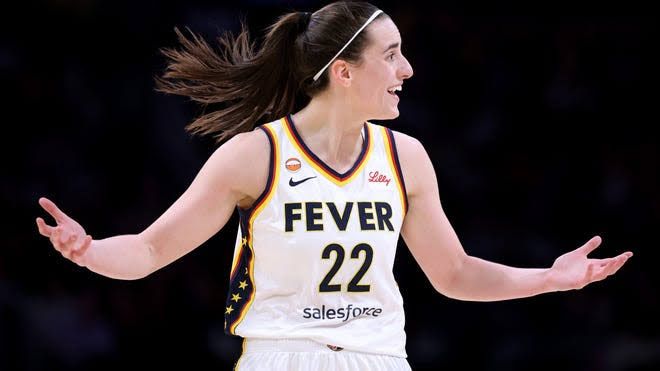 Caitlin Clark stands on the court during a WNBA game while officials monitor the play.