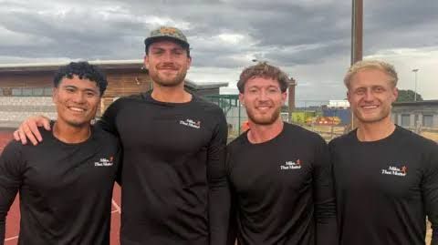 Four men in matching black tops with Miles That Matter logos stand on a running track in Lincoln.