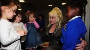 Dolly Parton speaking with children while holding a book, highlighting her long-term work for childhood literacy.