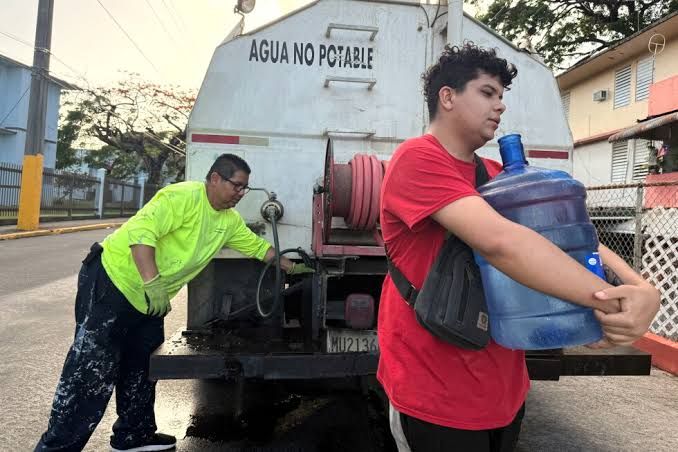 A resident in San Juan carries a five-gallon water jug to his apartment during a local water shortage.