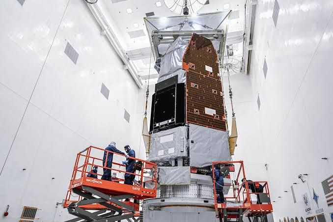 Engineers at Kennedy Space Center use a crane to position the Nancy Grace Roman Space Telescope on a work stand.