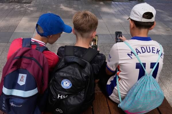 Three students sitting outside a school in Sydney, holding their smartphones while using the devices.