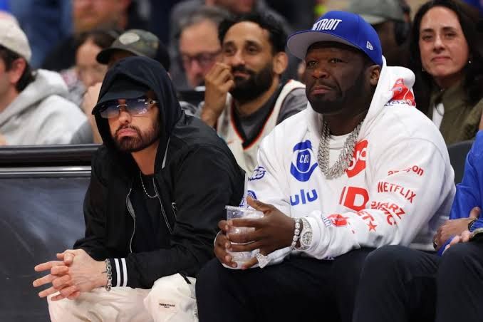 50 Cent and Eminem standing together at a basketball game at Little Caesars Arena in Detroit.
