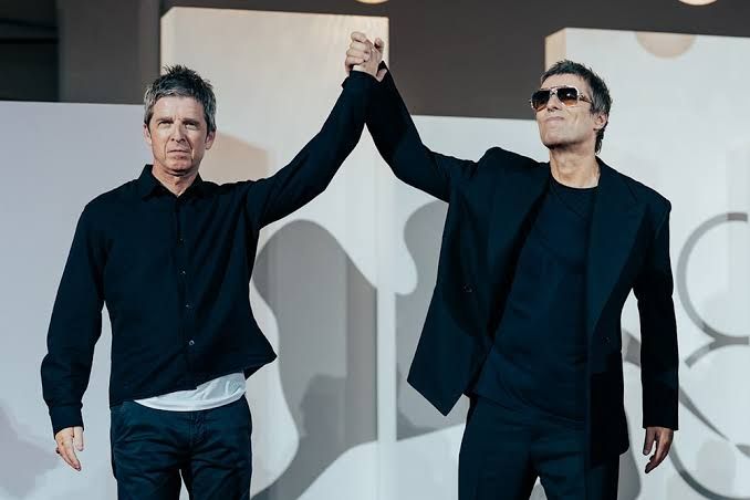 Liam and Noel Gallagher hold hands and wave to the crowd during the premiere of their Oasis documentary in Venice.