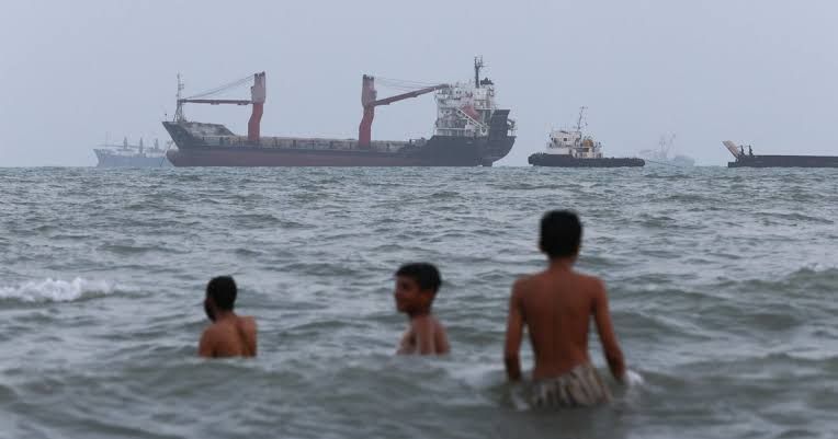An Iranian naval vessel patrolling near the Strait of Hormuz with cargo ships visible in the distance during the blockade.