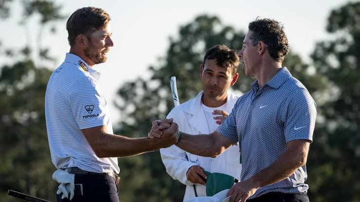 Sam Burns and Rory McIlroy walking on the course during a 2026 major championship golf tournament.