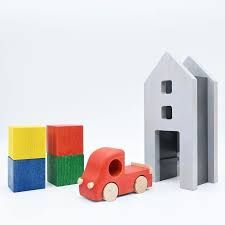 A wooden Tuminy toy truck sits on a flat surface next to small blocks representing cargo, showing its unloading mechanism.