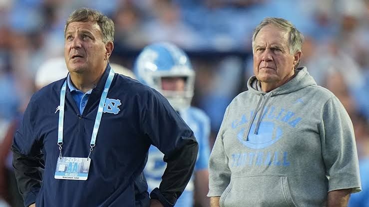 Bill Belichick and Michael Lombardi standing on the field during a North Carolina football game.