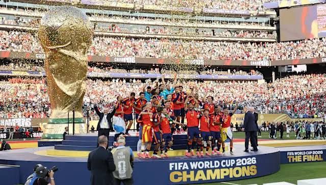 Spain national soccer team players lifting the World Cup trophy while President Donald Trump stands near the stage edge.