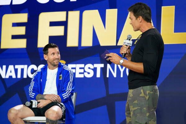 Lionel Messi listens to Tom Brady during a press conference in New York ahead of the 2026 World Cup final.