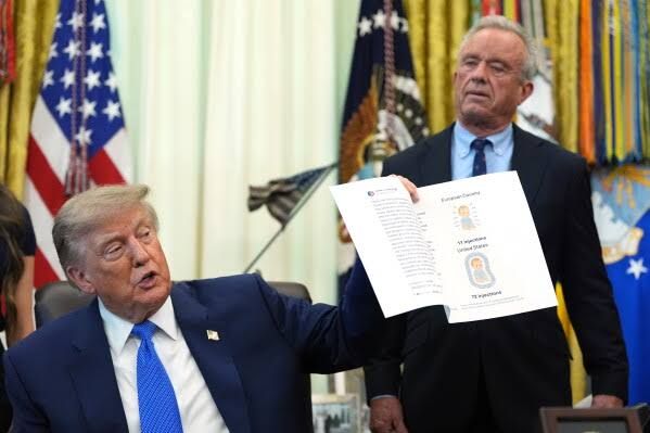 President Donald Trump signs an executive order on vaccines in the Oval Office as HHS Secretary Robert F. Kennedy Jr. watches.