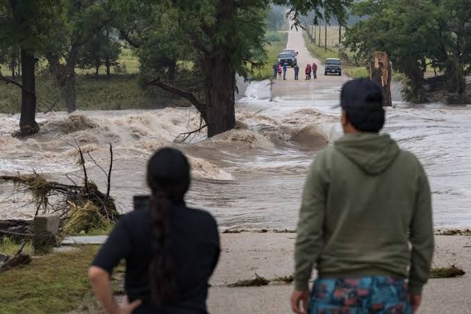 Onlookers watch as floodwaters cover East Lane Valley Road in Comfort, Texas, following heavy regional rainfall.