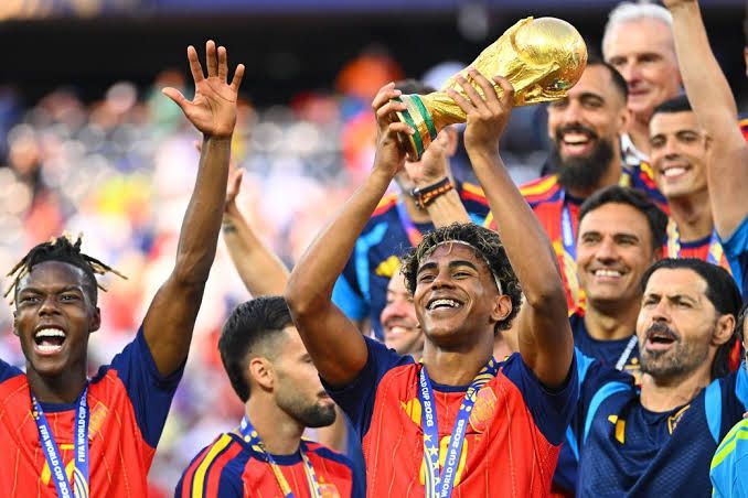 Spain national team players celebrating with the World Cup trophy on the pitch after the 2026 tournament final.