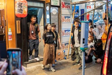 An independent bookstore employee is escorted by plainclothes officers near a shopfront during Hong Kong security raids.