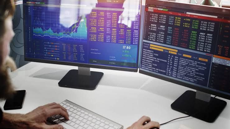 A trader monitors multiple financial screens displaying charts as oil prices rise following international conflict.