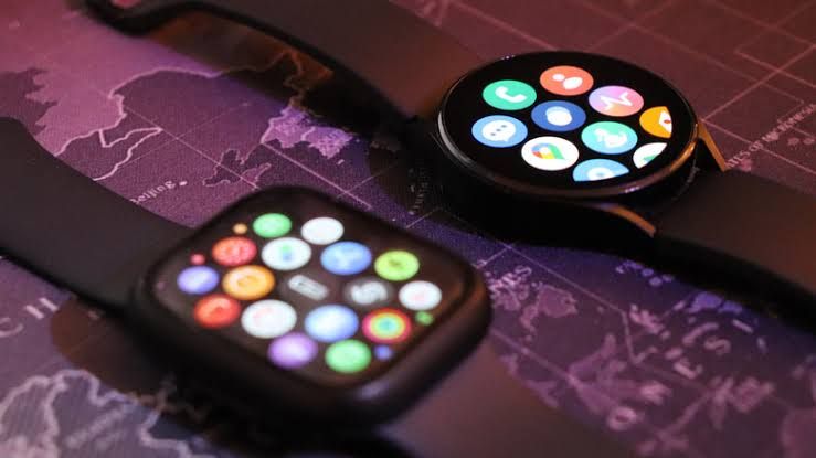 Apple Watch and Samsung Galaxy Watch placed side by side on a neutral surface.