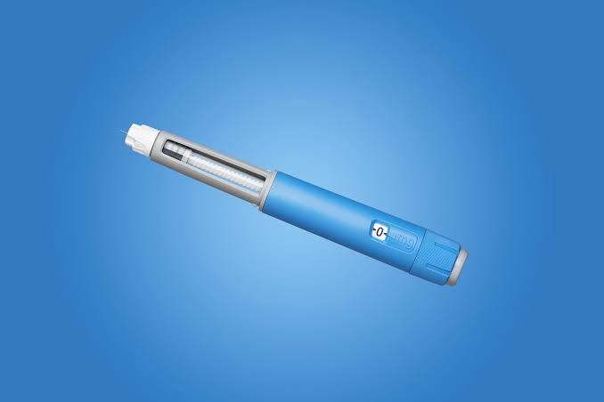 A medical dosing pen for weight-loss medication positioned on a blue surface.