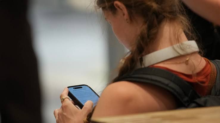 An 18-year-old using a smartphone to navigate social media applications while sitting in a modern environment.