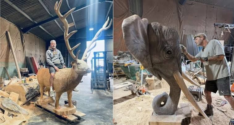 Artist Simon Bogg stands next to his carved wooden stag and elephant sculptures in his outdoor workshop.