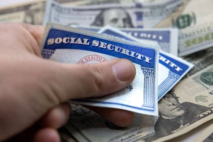 Close up of a person looking at a retirement calculator on a laptop screen with Social Security documents nearby.