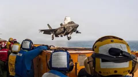 US fighter jet in flight near the USS Boxer in the Strait of Hormuz during ongoing military operations.